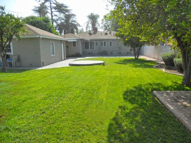 House view from far corner of back yard, complete with elevated spa pad, fruit trees, garden area, vinyl fencing, and RV access gate.