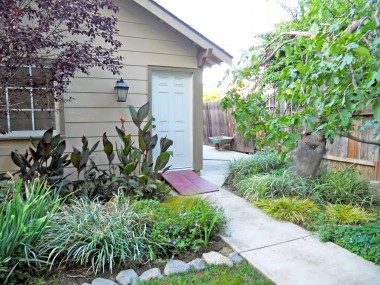 Another view of garage with lush landscaping, mature and producing fig tree, and cemented side yard which could be utilized for boat or small RV parking.