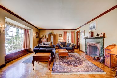 Large living room with mahogany moulding, large window seat with hidden storage, and a gas/wood-burning fireplace.
