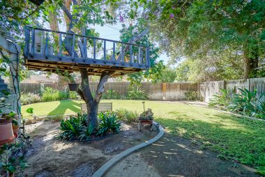 Back section of pool-sized yard completely landscaped with tree fort, mow curb, mature shade trees, and gate to alley.