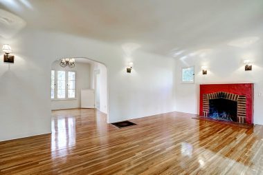 View of gorgeous living room with coved ceiling, fireplace, sconce lighting, and recently refinished original hardwood floors. View into the formal dining room with Dutch door leading to the kitchen.