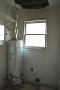 Laundry room with water heater and damage to ceiling.