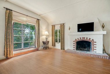 Living room with original hardwood floors, large front window, and coved ceiling.