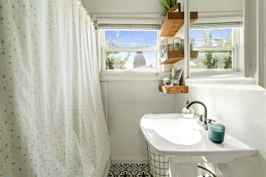 Bathroom with shower in tub, pedestal sink, floating shelves, and newer flooring.