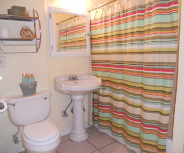 Remodeled bathroom with glass doors behind shower curtain, pedestal sink, tile flooring. Access to bathroom from master bedroom and hallway.