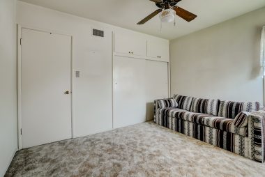 Back bedroom with hardwood floors under carpeting, spacious closet, and ceiling fan.