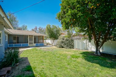 Pool-size back yard with orange and avocado trees, white vinyl fence, and view of screened-in bonus room.