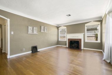 Living room with hardwood floors, two toned paint, decorative vintage floor vents, and gas & wood-burning fireplace.