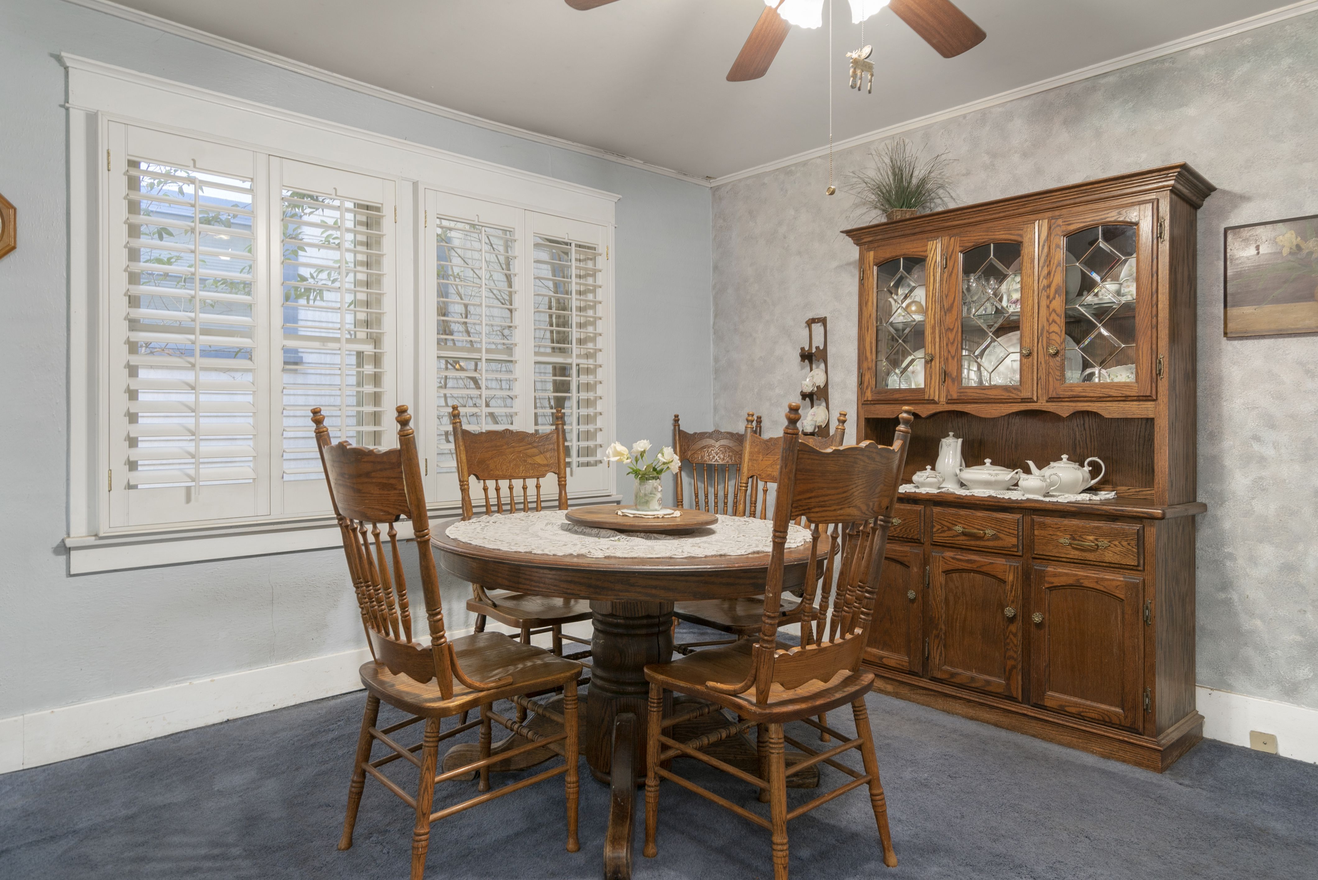 Formal dining area with ceiling fan and plantation shutters over double pane windows.