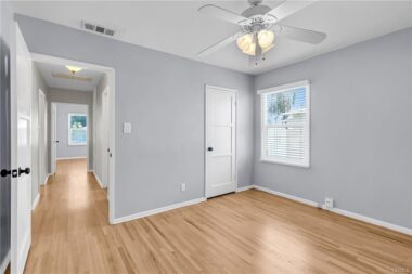Unstaged back bedroom with ceiling fan, hardwood floors, new window blinds, double pane windows, and view into the hallway.
