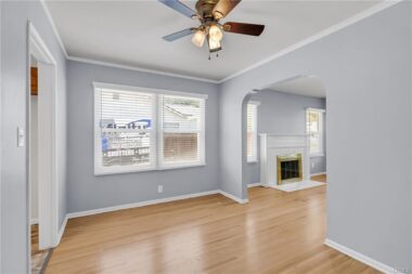 Unstaged photo of formal dining room with hardwood floors, new window blinds, ceiling fan, and view into the living room.