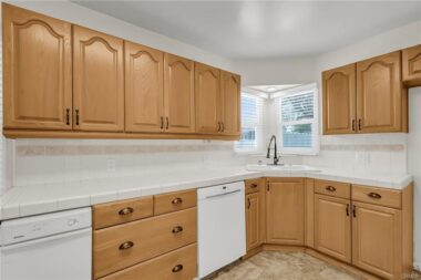 Remodeled kitchen with tile counter tops, lots of cabinetry, corner sink, dishwasher and trash compactor.