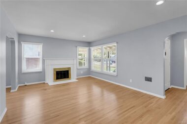 Unstaged photo of living room with hardwoof floors, recessed lighting, fireplace, double pane windows, new window blinds, and fresh paint.
