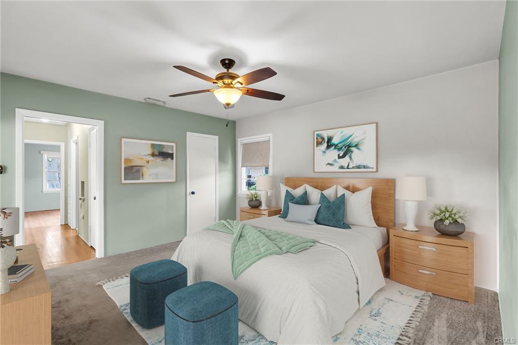 Primary bedroom suite with walk-in closet, ceiling fan, and hardwood flooring under carpeting with view into the hallway. Virtually Staged.