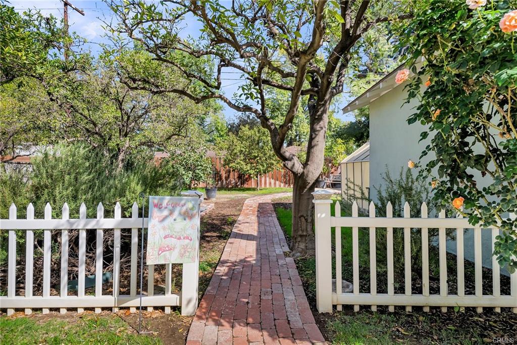 White picket fence whimsically leading to the garden area of the beautiful yard, lined with roses and an aromatic rosemary bush.