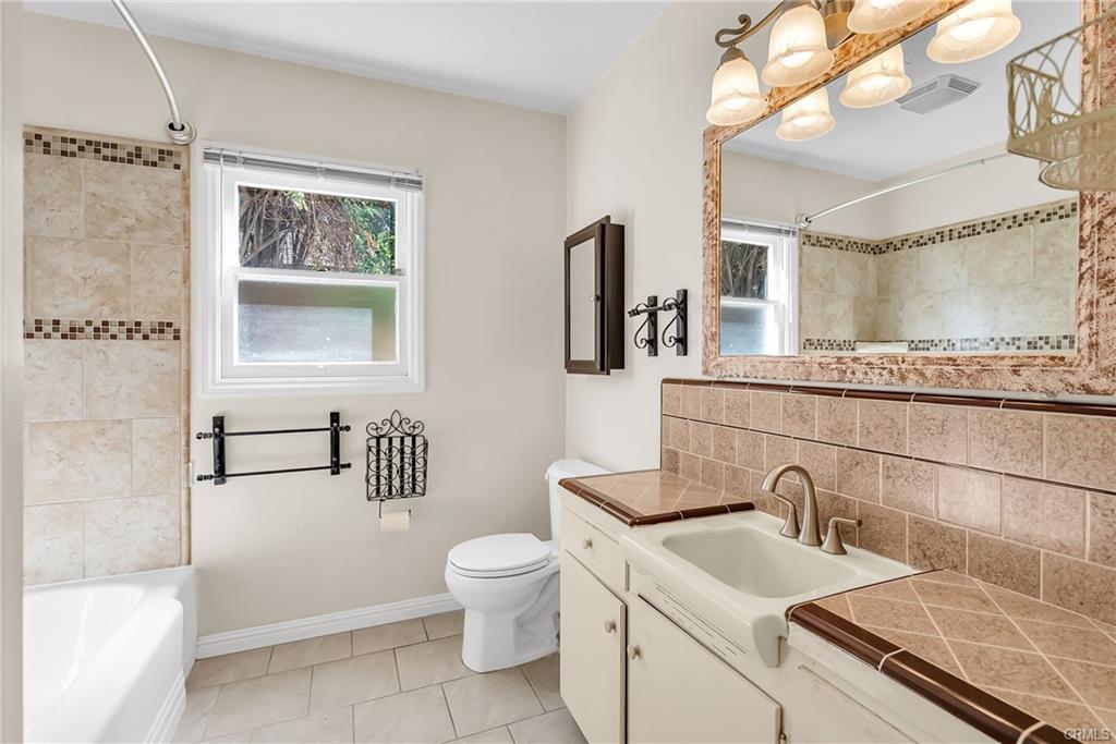 Hallway bathroom with remodeled shower/tub space, with vintage sink and counter top and new faucet. Tile flooring, and pull-out shelving in linen closet.