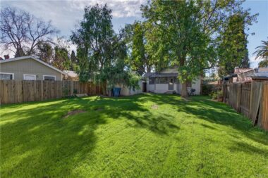 View of house and garage from far back corner of large enclosed yard. Sprinkler system has not worked in a while, so new owner will need to update the system.