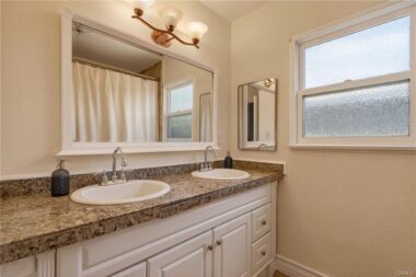 Hallway bathroom with dual sinks and a spa tub with shower.
